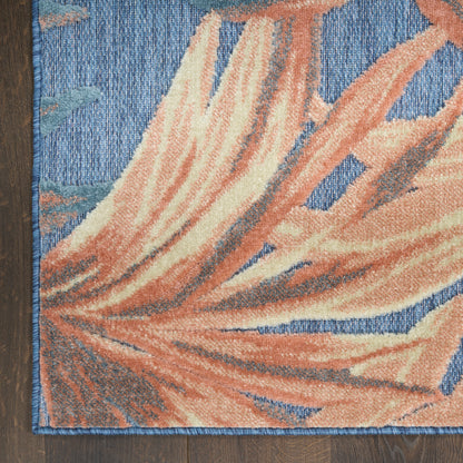 Decorative rug with a large orange coral leaf motif on a blue backdrop; blue edge stitching, placed on a wood floor.