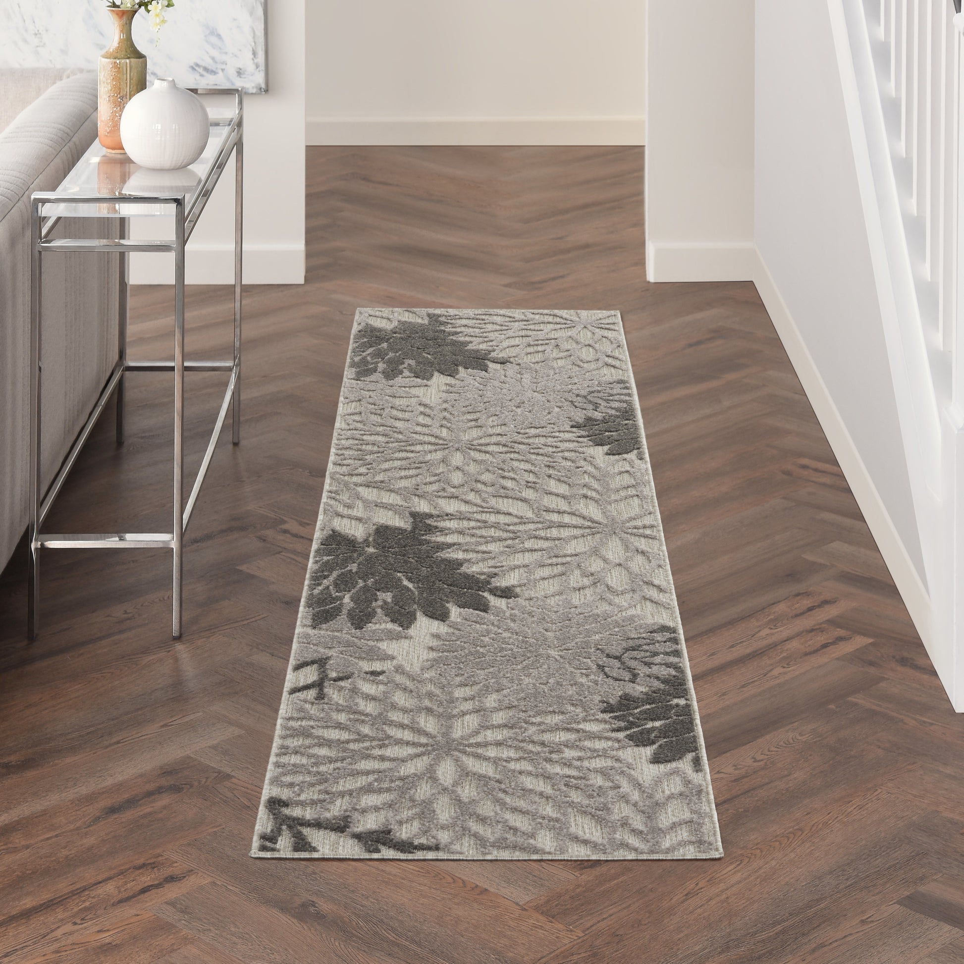 Gray botanical-pattern runner rug with soft pile in a hallway, beside a glass console table on dark wood flooring