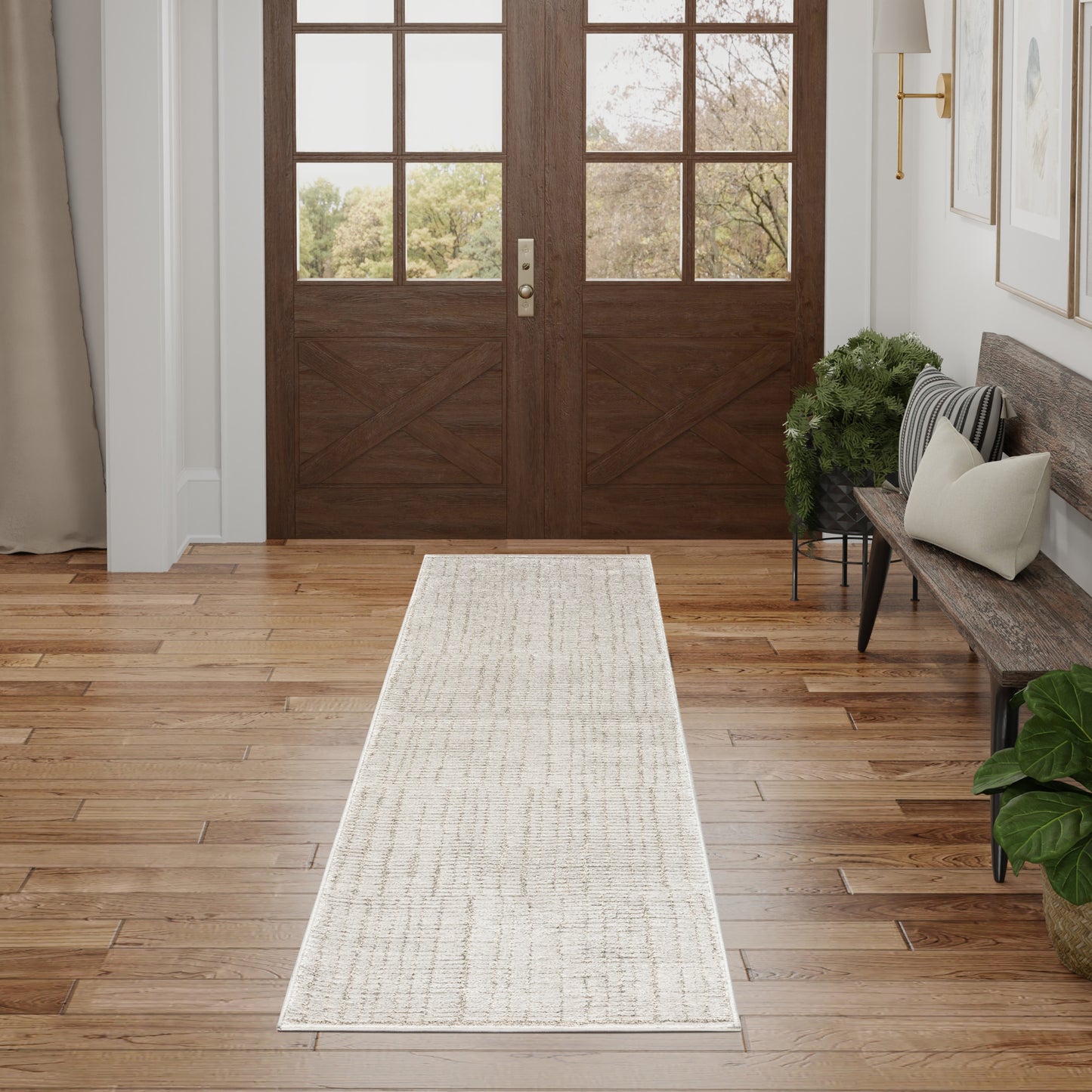 Long cream runner rug on hardwood floor in entryway with double wood doors and glass panes, bench with cushions and plants.