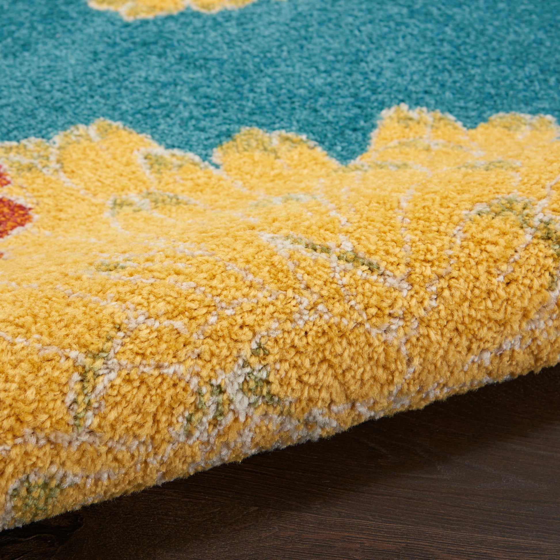 Close-up of a yellow shag area rug with teal blue field, thick plush pile, rolled edge on dark wood floor