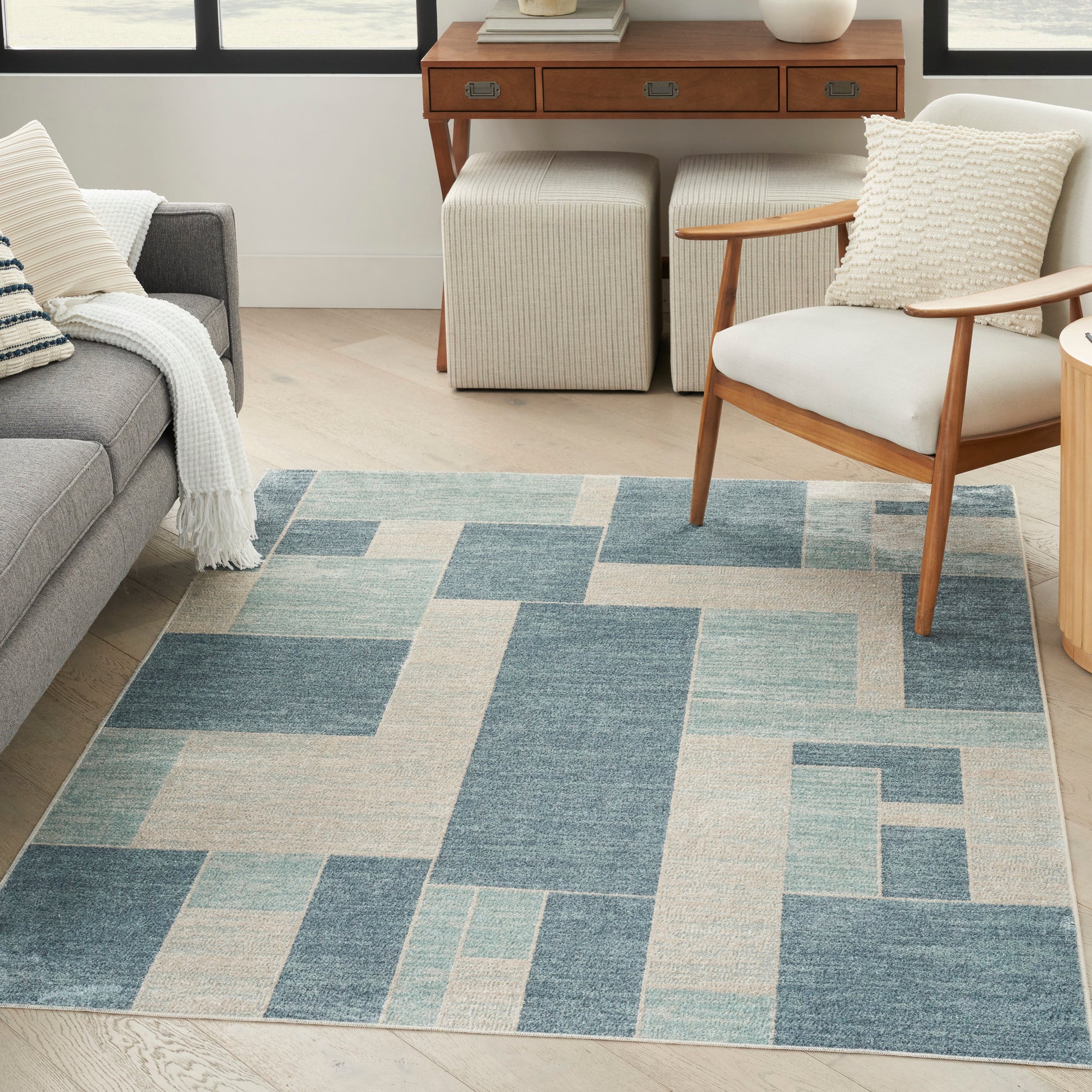 Geometric blue and beige area rug in a living room with a gray sofa, knit throw, mid-century chair, and wooden console.