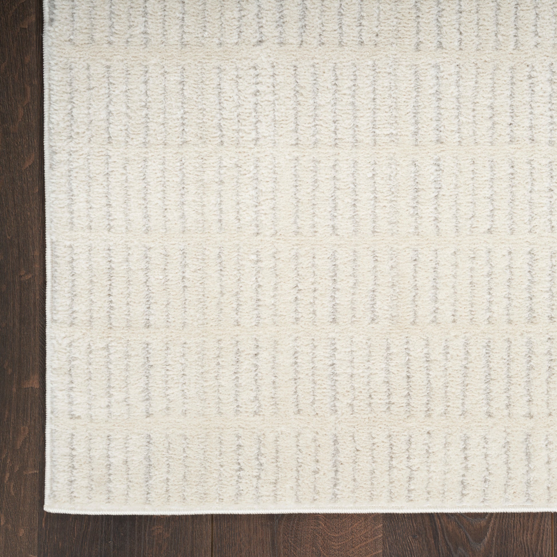 Ivory textured area rug with raised vertical stripe pattern and white border on dark hardwood floor.