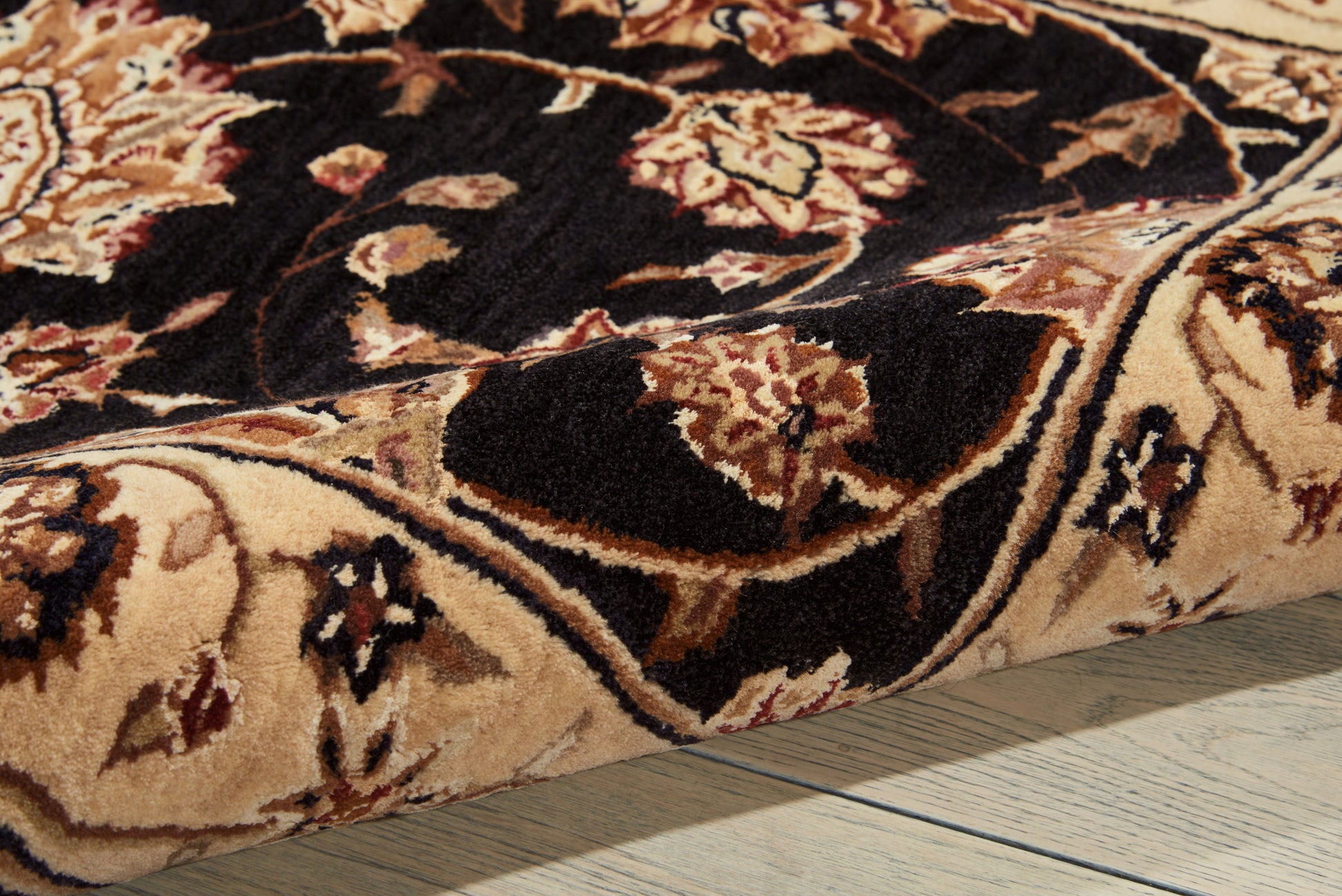 Close-up of oriental floral rug with beige, cream, brown and black colors and a thick pile on a wooden floor.