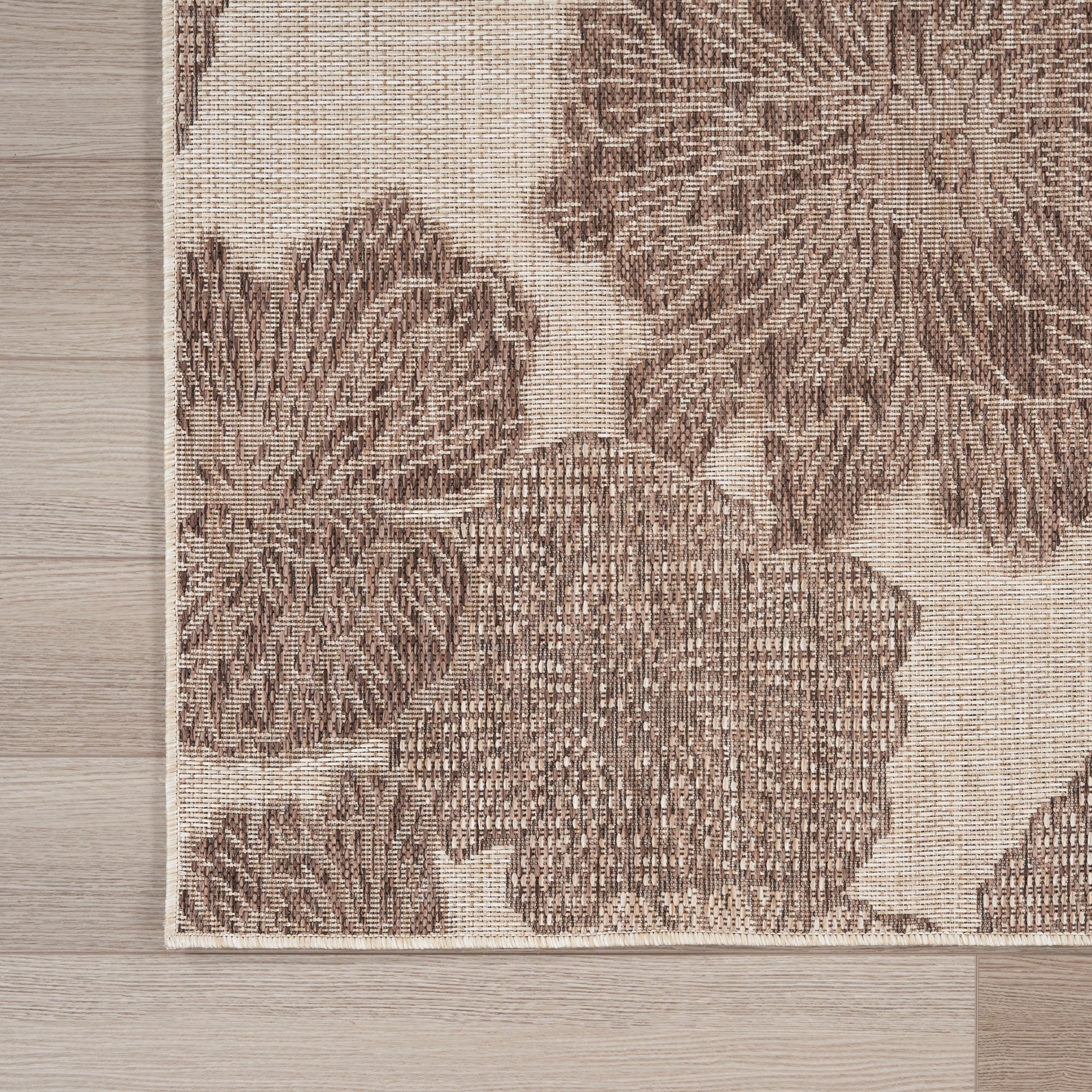 Beige woven rug with dark brown large floral pattern, 3' x 5', edge visible on light wood floor.