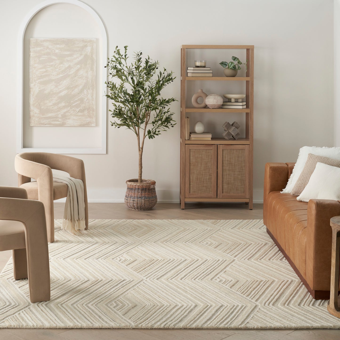 Neutral-toned living room with tan boucle chairs, brown leather sofa, woven cabinet, potted tree, and geometric beige rug.