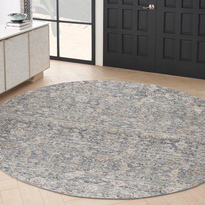 Round blue-gray area rug with ivory-gold pattern in entryway, near black paneled doors and light wood floor.