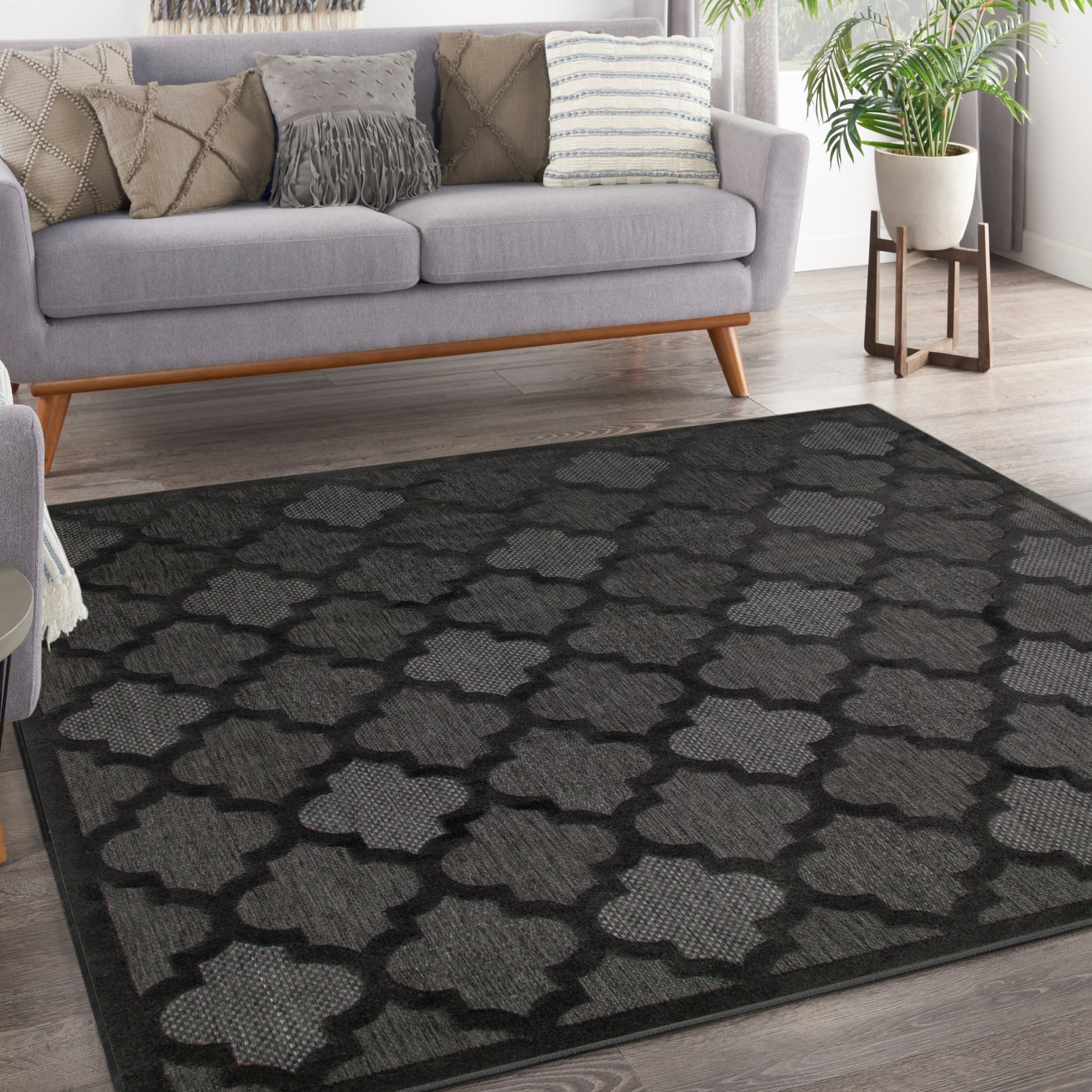 Rectangular woven charcoal rug with light-gray trellis pattern, modern living room under a gray sofa.