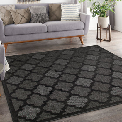 Rectangular woven charcoal rug with light-gray trellis pattern, modern living room under a gray sofa.