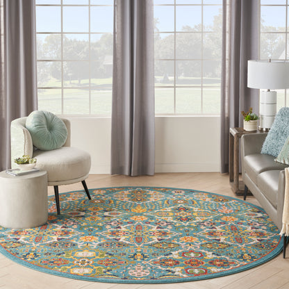 Round teal rug with a colorful floral pattern in a cozy living room with a beige curved chair, gray curtains, and sofa.