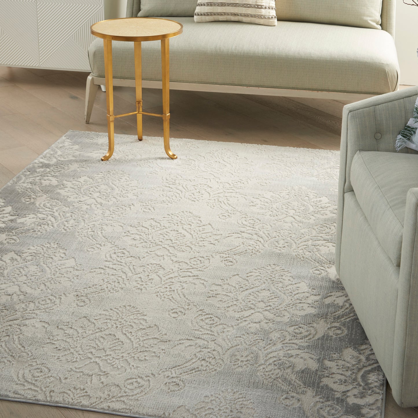 Light gray damask rug on wood floor with a round wooden side table and pale beige sofa in a cozy living room.