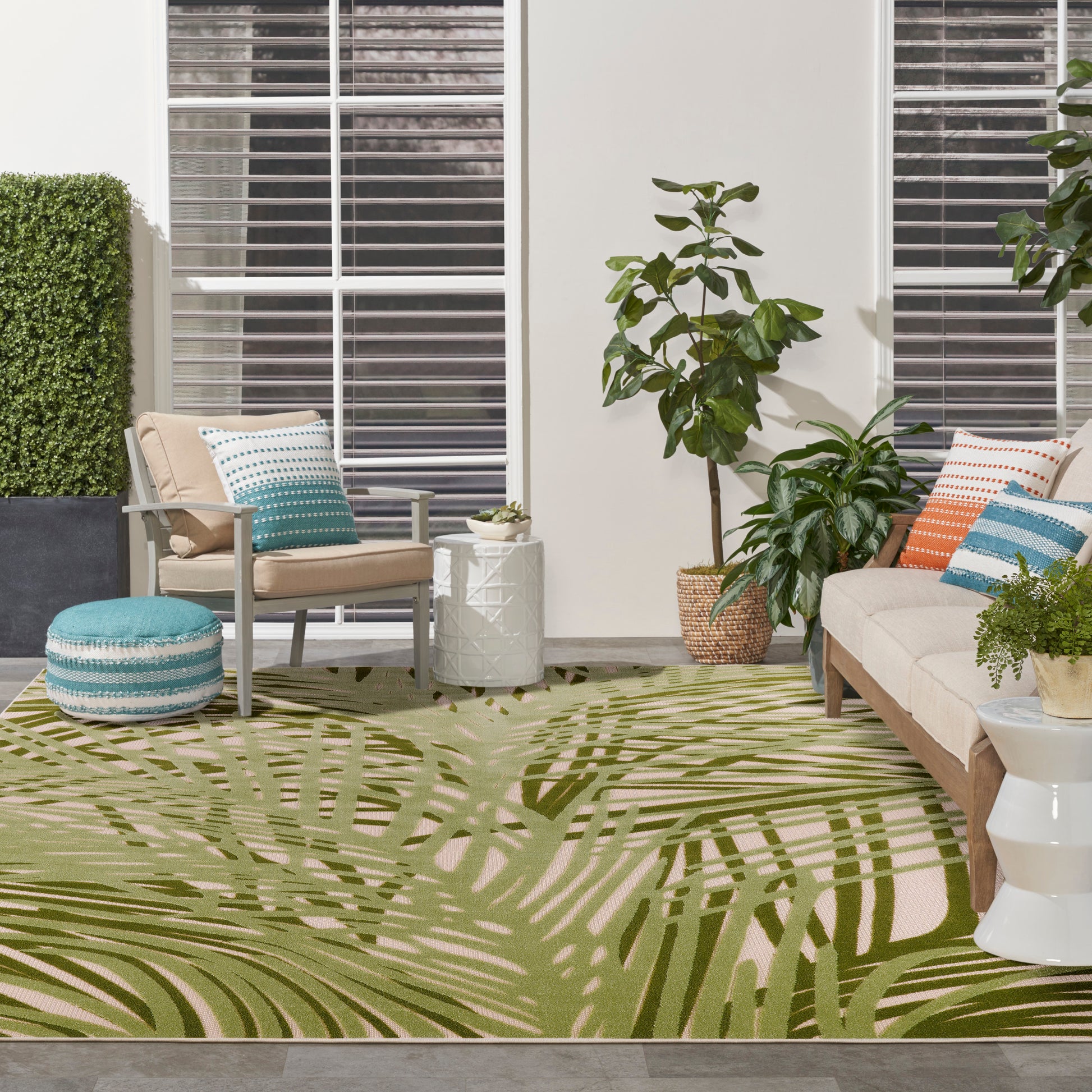 Tropical palm-leaf rug in olive green and tan under beige seating with blue striped and orange cushions and potted plants.