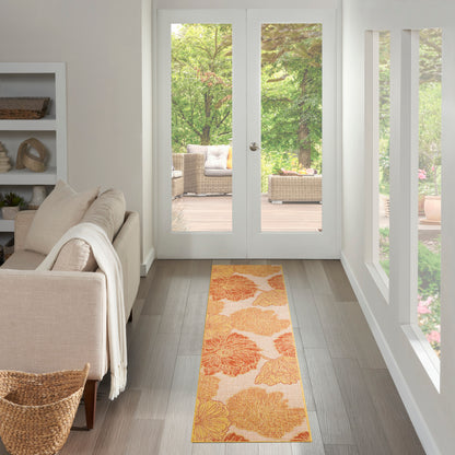 Long orange floral rug runner on light wood floor in a bright beige living room with a sofa and glass doors to a wicker patio