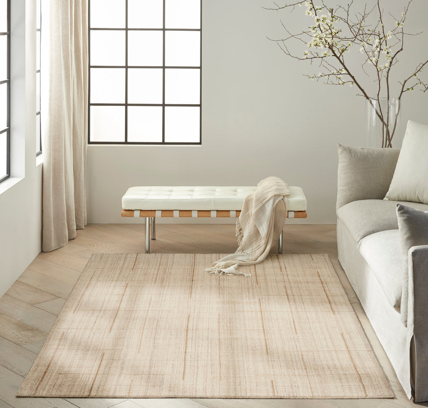 Bright minimalist living room with tufted white bench, pale beige rug, light sofa, sheer curtains, and a bare branch decor.