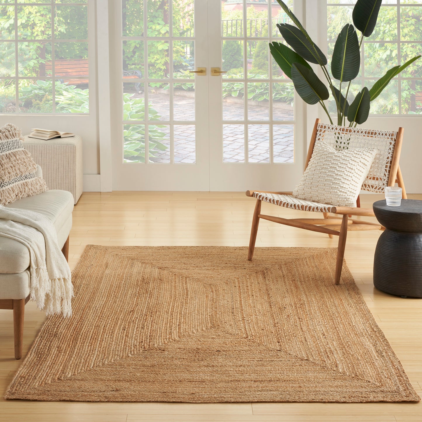 Rectangular natural jute rug in a light wood living room with a woven chair, cream sofa, and large green plant.