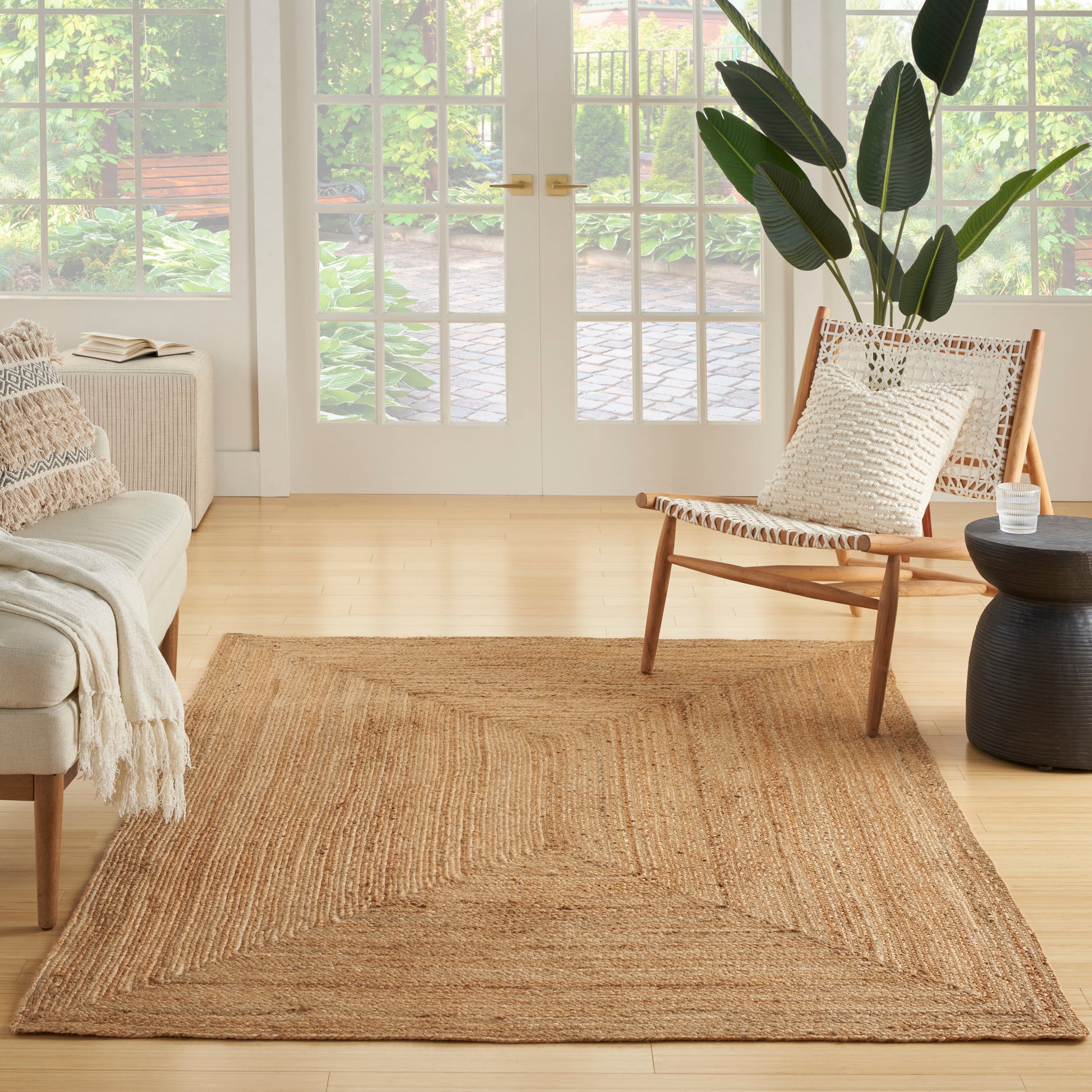 Rectangular natural jute rug in a light wood living room with a woven chair, cream sofa, and large green plant.