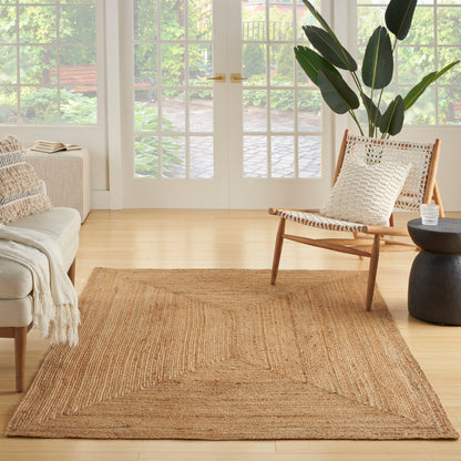 Rectangular natural jute rug in a light wood living room with a woven chair, cream sofa, and large green plant.
