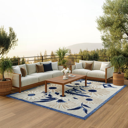 Blue floral rug on a deck with beige cushioned sectional, wooden coffee table, and potted plants.