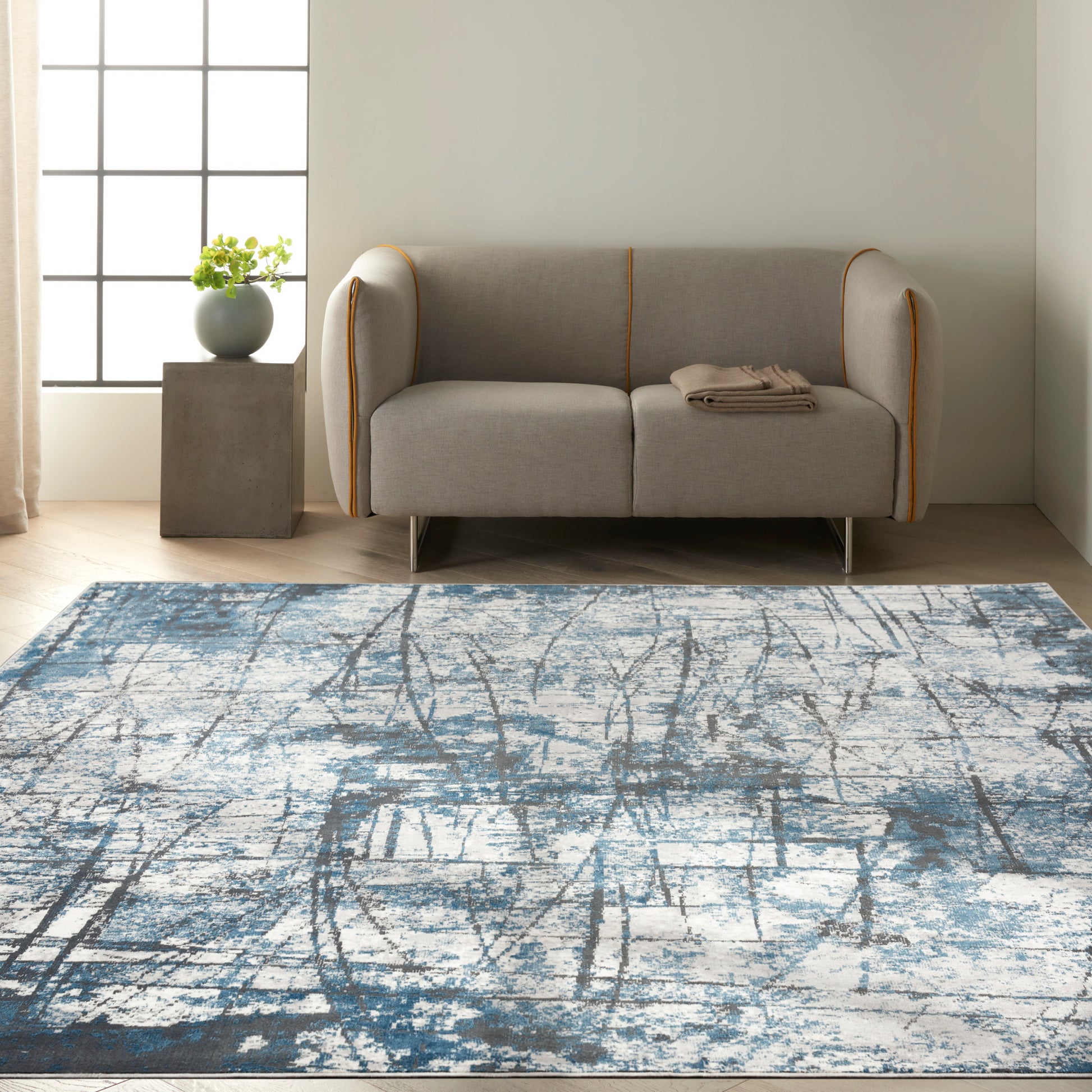 Gray fabric sofa with orange piping and metal legs, folded beige throw, on a blue-gray abstract rug in a modern living room.