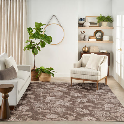 Brown floral area rug in a neutral living room with a beige striped armchair, light sofa, greenery & wooden shelves.