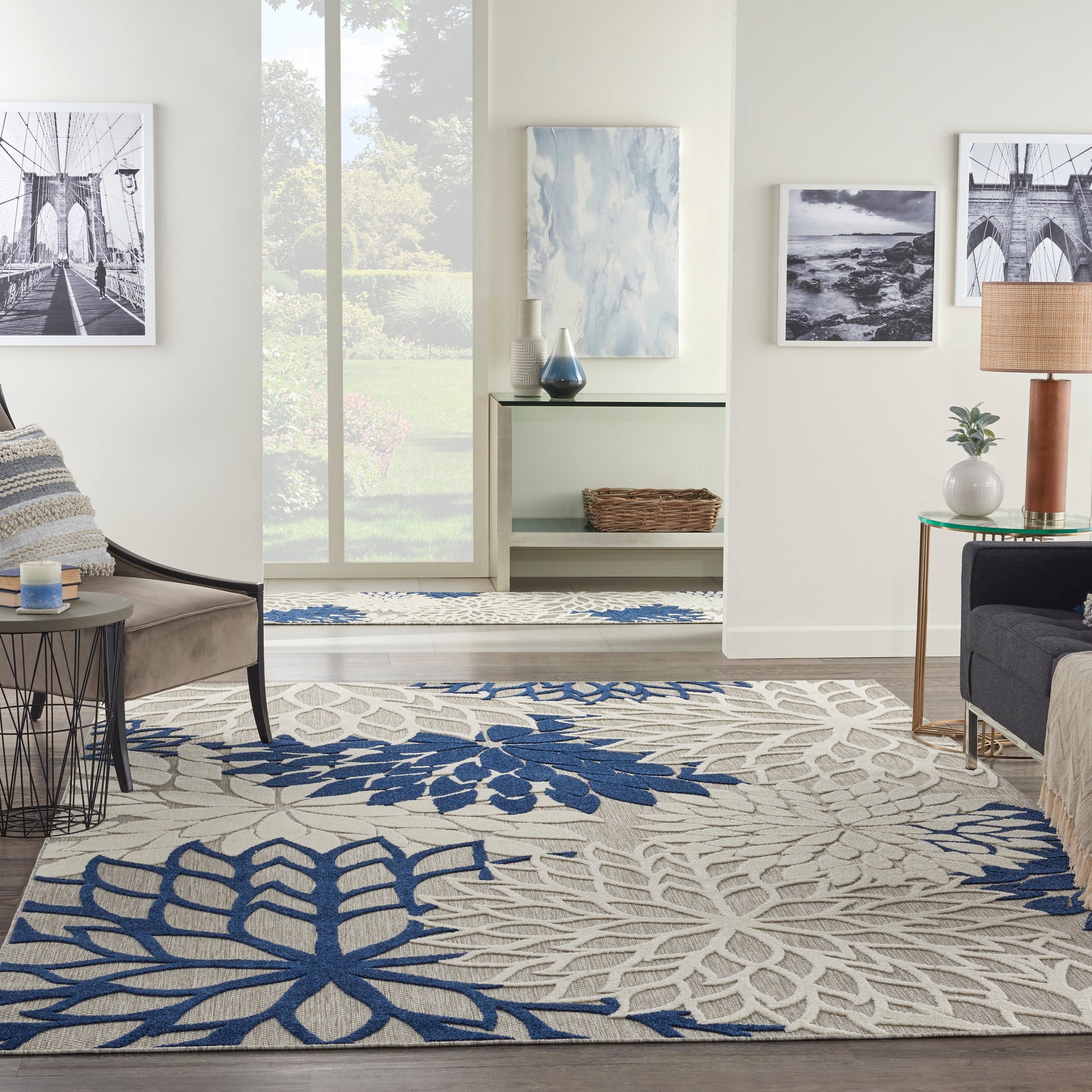 Living room with cream area rug featuring bold blue botanical patterns, beige seating, glass tables, and wall art.
