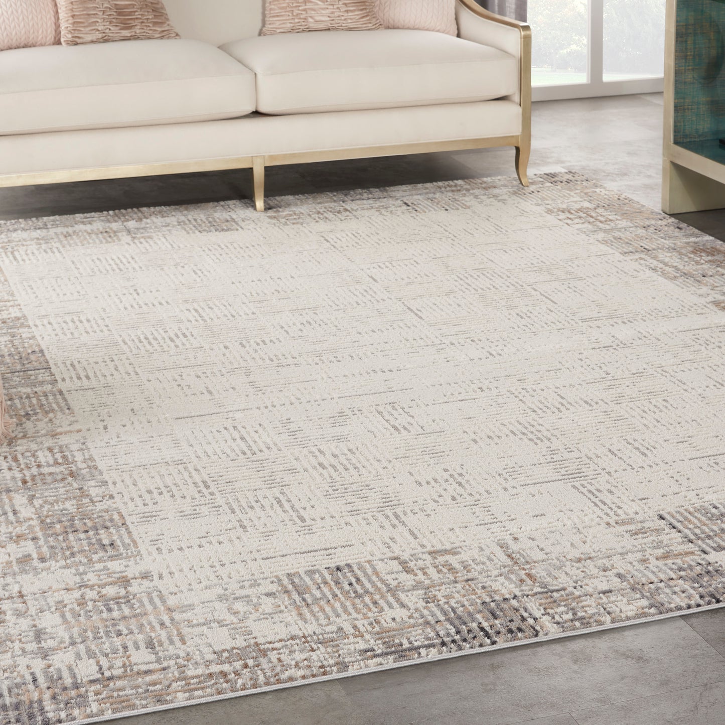 Neutral beige area rug with abstract taupe pattern under a cream sofa with a light wood frame.