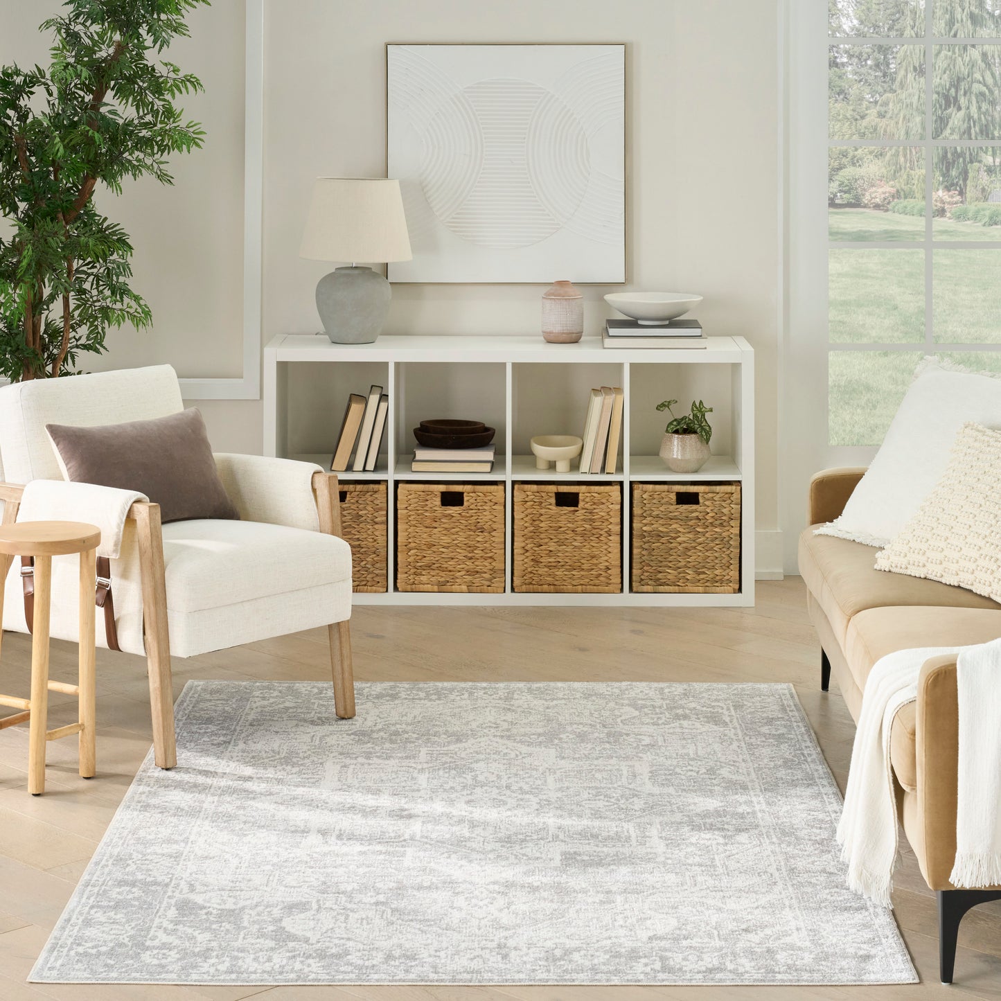 Neutral living room with white cubby storage and woven baskets, beige seating, gray patterned rug, large window view.