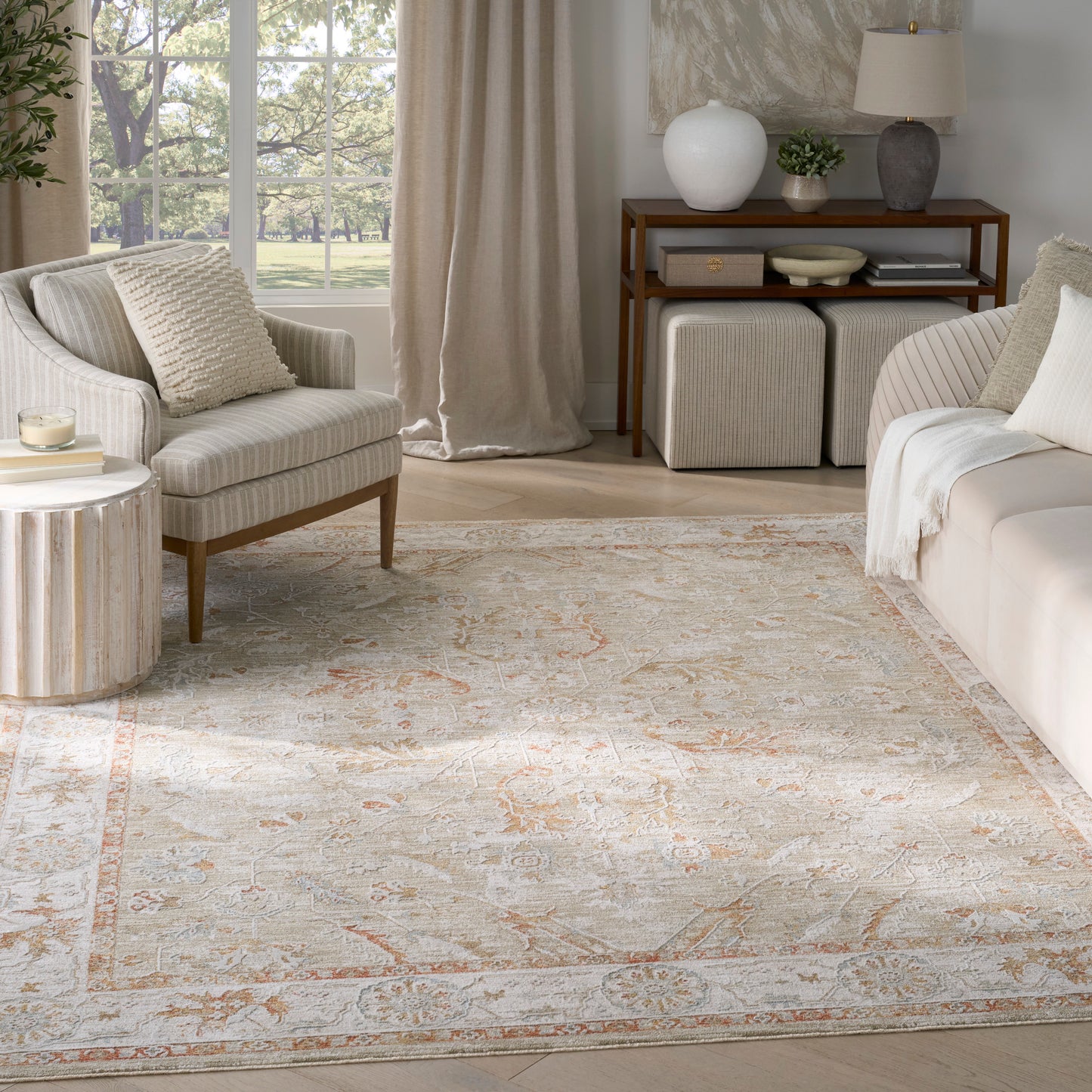 Neutral living room with cream striped armchair, beige sofa, round wood side table, and ivory rug with peach accents.