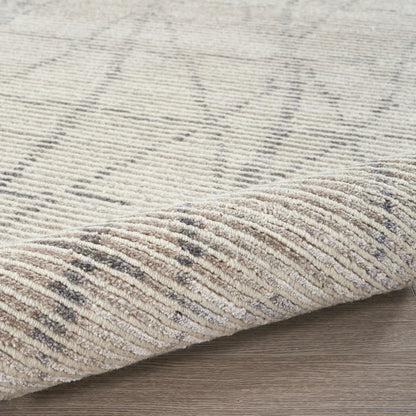 Beige woven area rug with subtle blue geometric pattern, folded corner on a wooden floor.