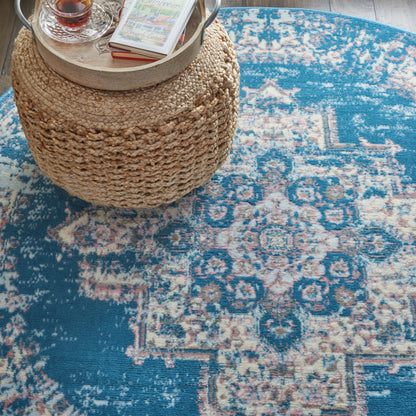 Round woven rattan ottoman with a wooden tray, glass teacup and books, on a blue oriental rug.