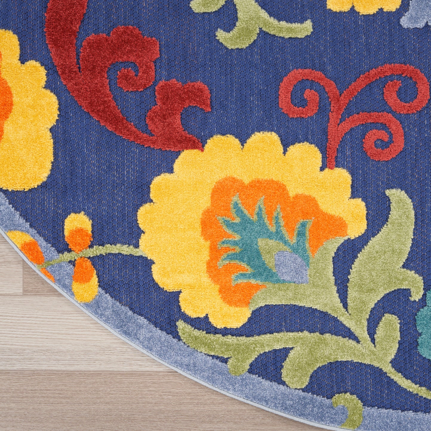 Round blue rug with bright yellow and orange flowers, red swirls, green vines, and pale gray edging on wood floor.