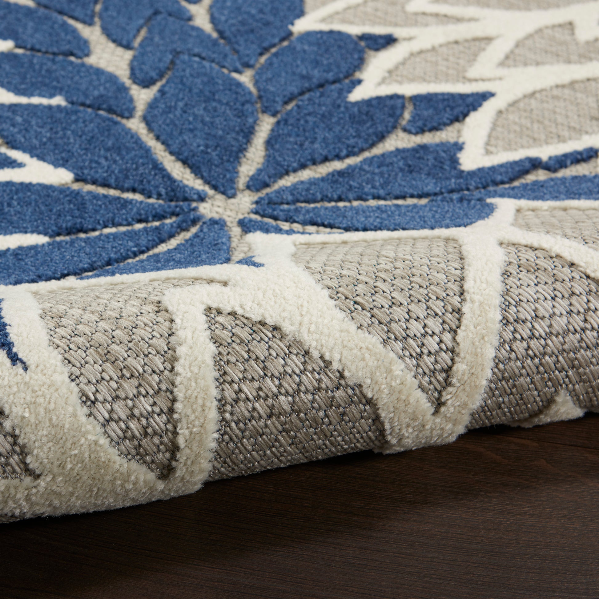 Blue floral area rug with cream border, plush textured pile and woven pattern on dark wood floor.