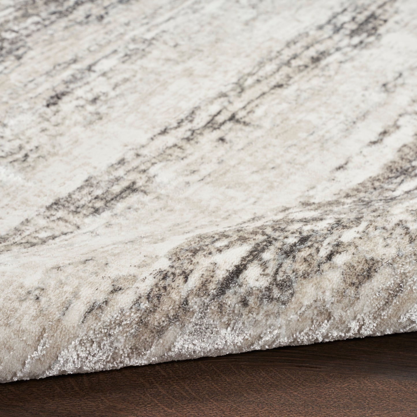 Cream and gray marbled plush area rug with a folded edge on dark wood floor.