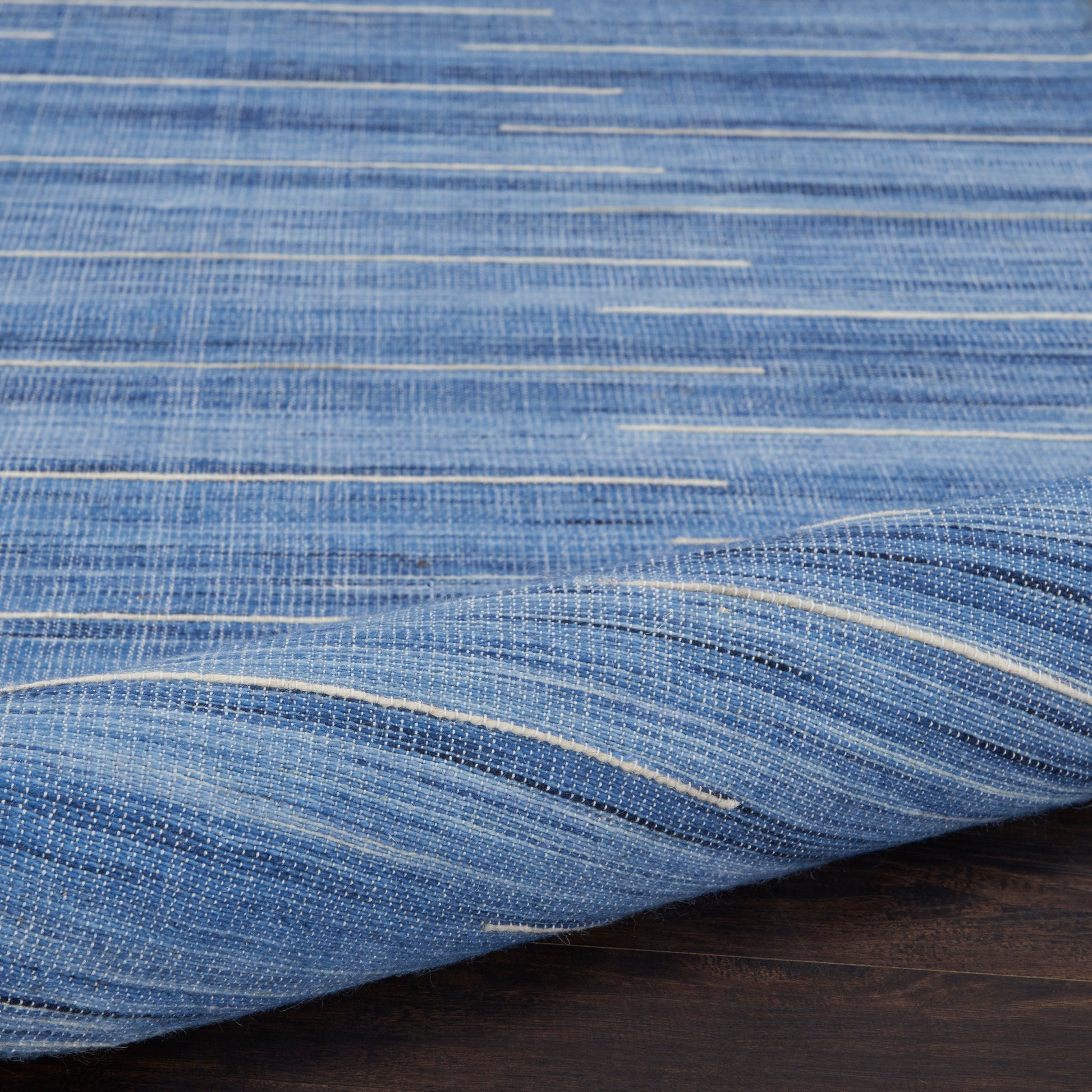 Blue woven linen-like fabric with white streaks, folded on dark wood surface.
