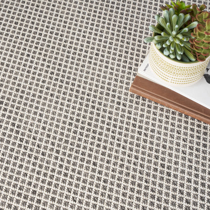 Neutral gray-beige woven rug with a glimpsed potted succulent on it beside a wooden table.