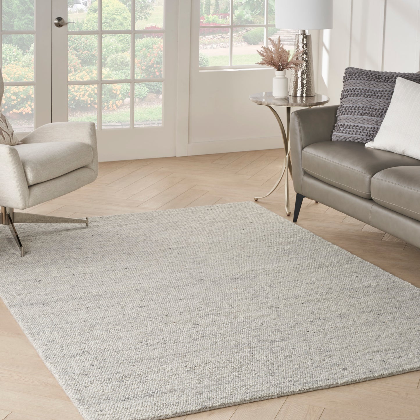 Light gray textured woven rectangular area rug in a modern living room with beige armchair and gray sofa.