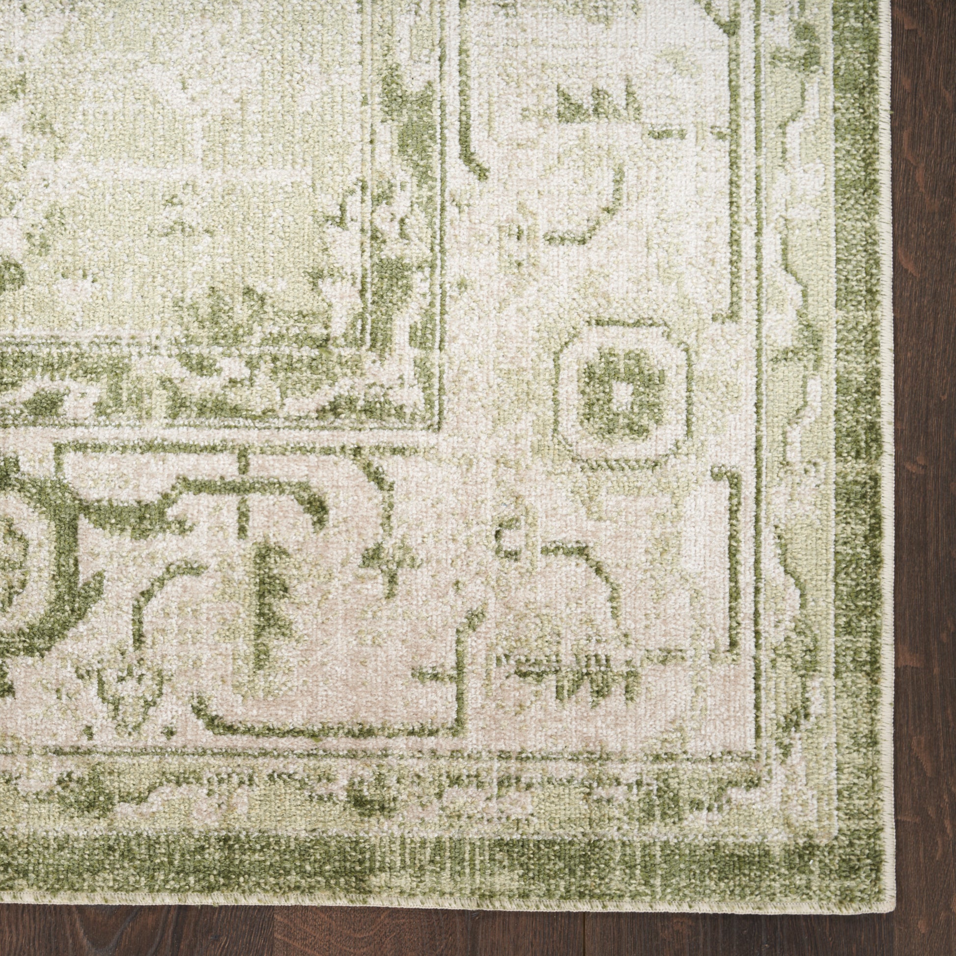 Olive-green bordered cream oriental rug on dark wood floor, vintage floral medallion pattern, plush texture.