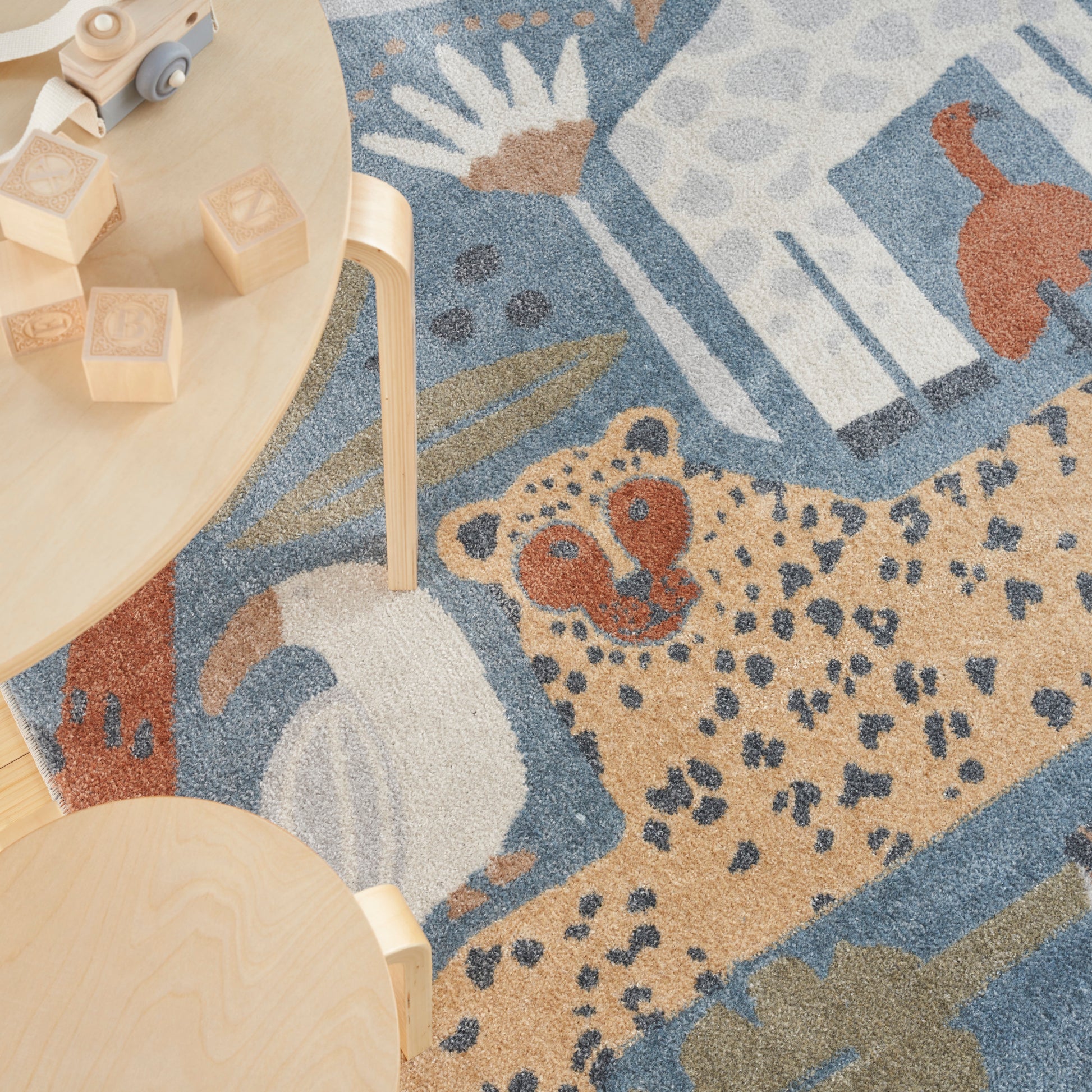 Wooden blocks and a small toy car on a round light table beside a blue-beige rug with a leopard print.