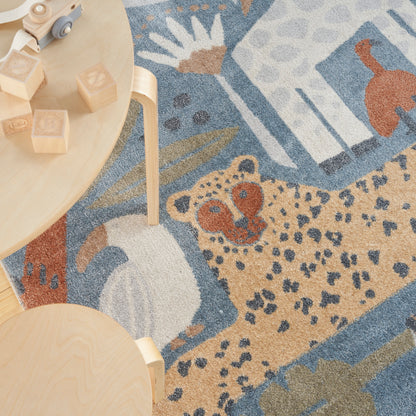 Wooden blocks and a small toy car on a round light table beside a blue-beige rug with a leopard print.