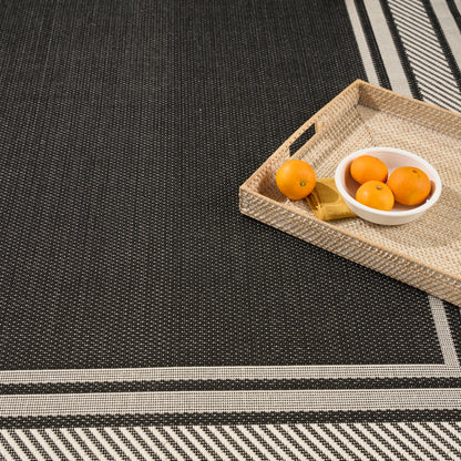 Beige woven rectangular rug with a white bowl of small oranges and a gold-wrapped item placed on a dark striped rug.