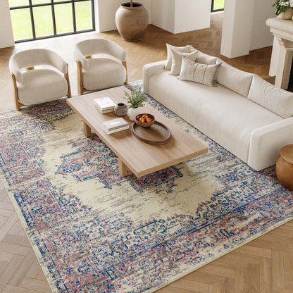 Neutral living room with beige sofa, two cream curved-arm chairs, light wood coffee table on a patterned beige-blue rug.