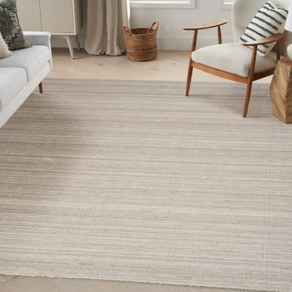 Neutral striped area rug in beige and taupe under a light living room with a mid-century chair, cream sofa, and woven basket.