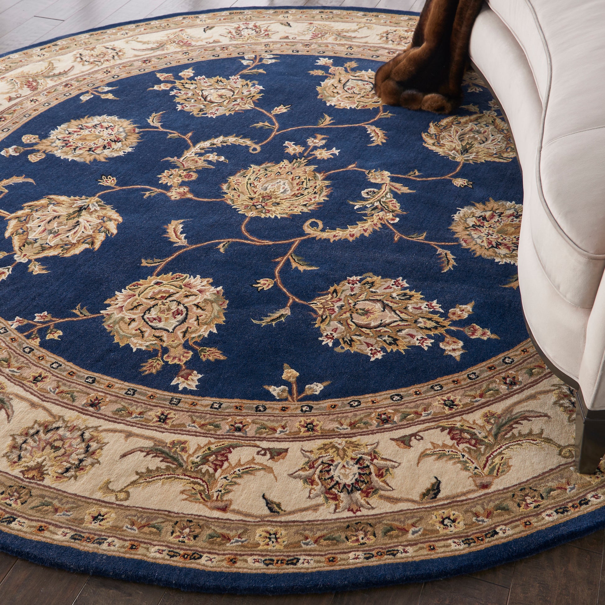 Round navy and cream oriental rug with gold floral medallions and scrolling border beneath a beige sofa.
