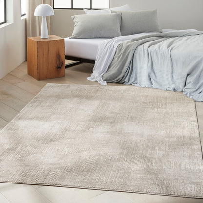 Beige textured area rug in a bright modern bedroom with light gray bedding, a wooden block nightstand, and a white dome lamp
