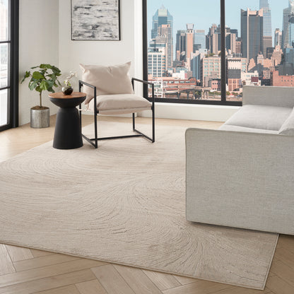Neutral living room with city view window, beige rug on light wood floor, cream armchair, black side table, plant, gray sofa.