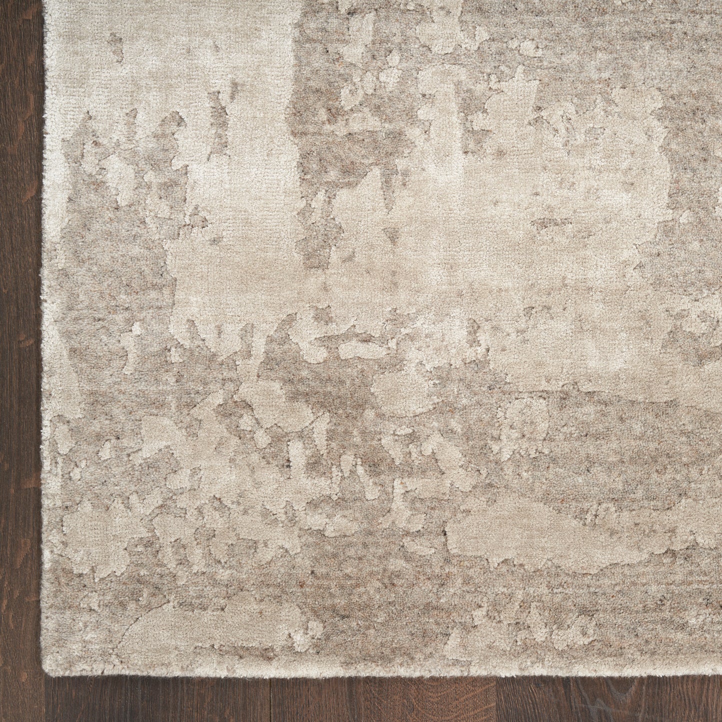Beige and cream distressed area rug with an abstract mottled pattern on dark hardwood floor, size 10' x 14'.