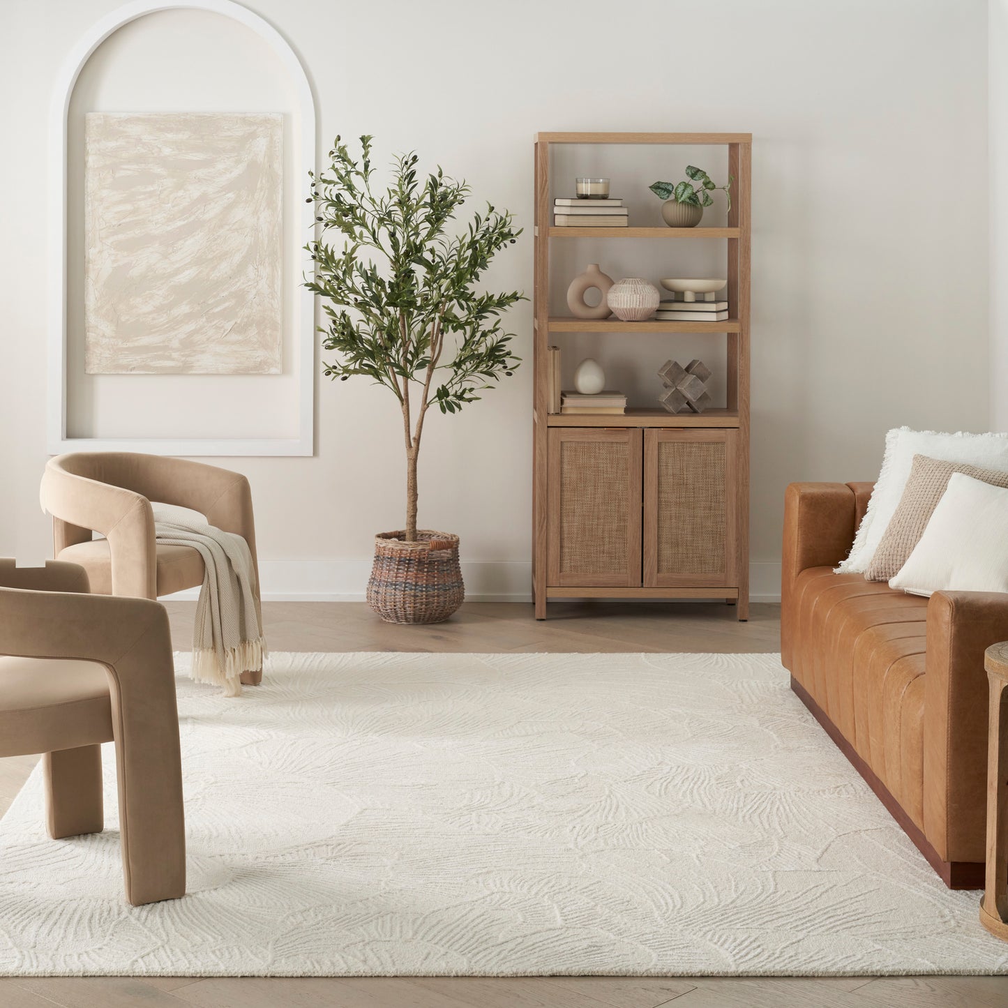 Neutral living room with beige armchairs, brown leather sofa, cream textured rug, tall potted tree, and woven wood cabinet.