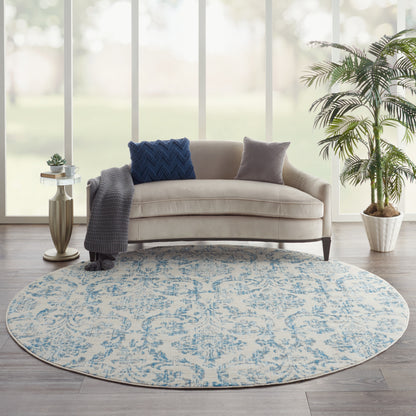 Round blue-and-beige patterned rug under beige curved sofa; gray throw, blue and gray pillows; modern living room