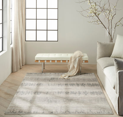 Neutral living room with cream tufted bench, beige throw, gray patterned rug, pale sofa, light wood floors, grid window.