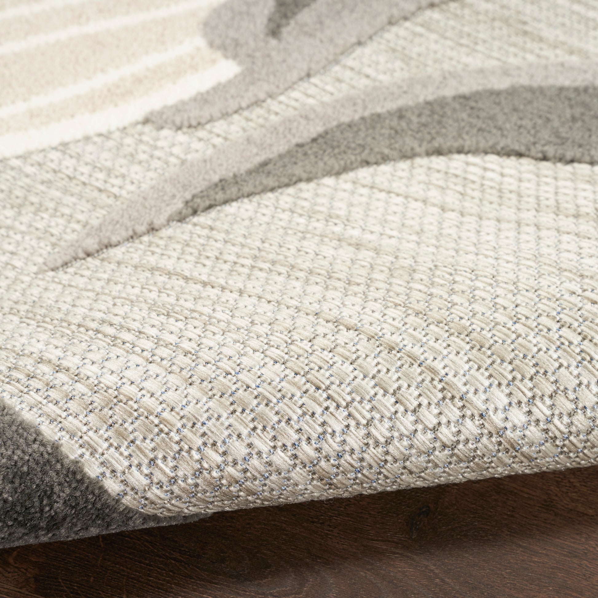Beige textured woven area rug with gray abstract pattern on dark wooden floor.