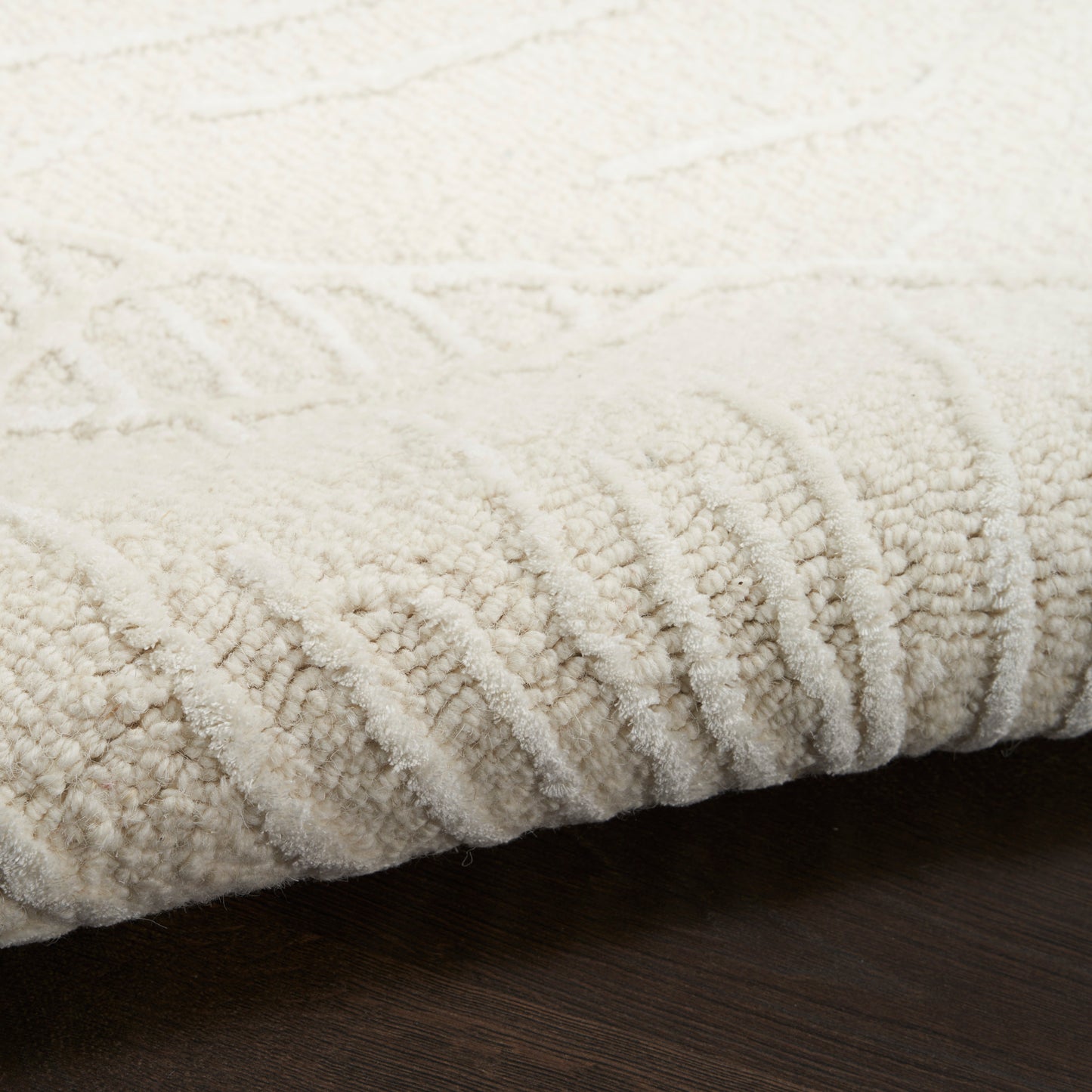 Cream ivory textured area rug with plush loop pile and ribbed edge on dark wood floor.